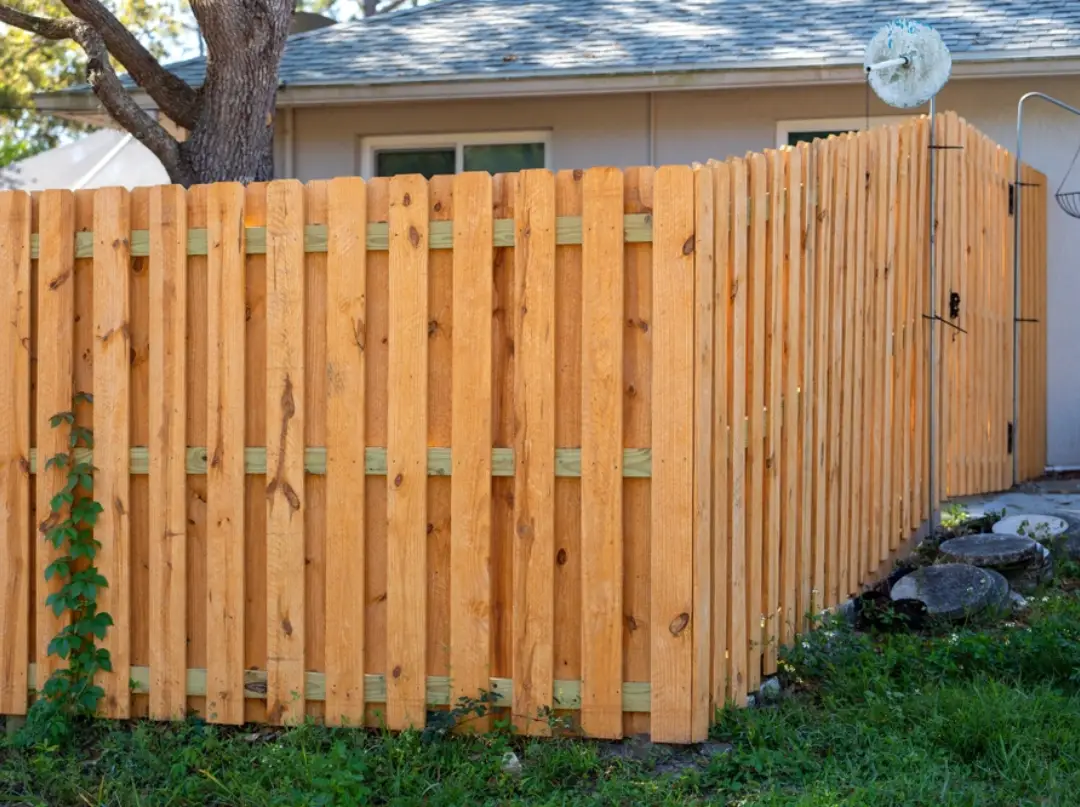 Traditional vertical wood plank privacy fence and gates in a residential backyard.