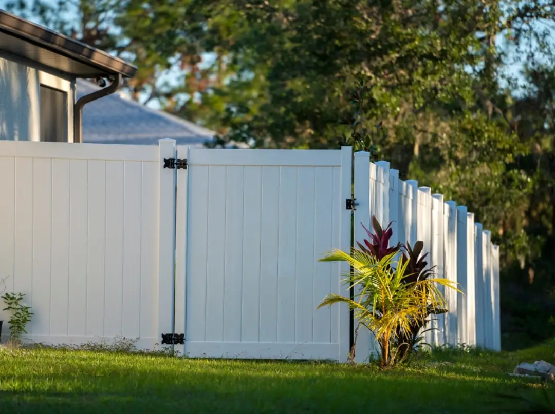 Side view of a white vinyl privacy fence and gates with a single-walk gate entry.