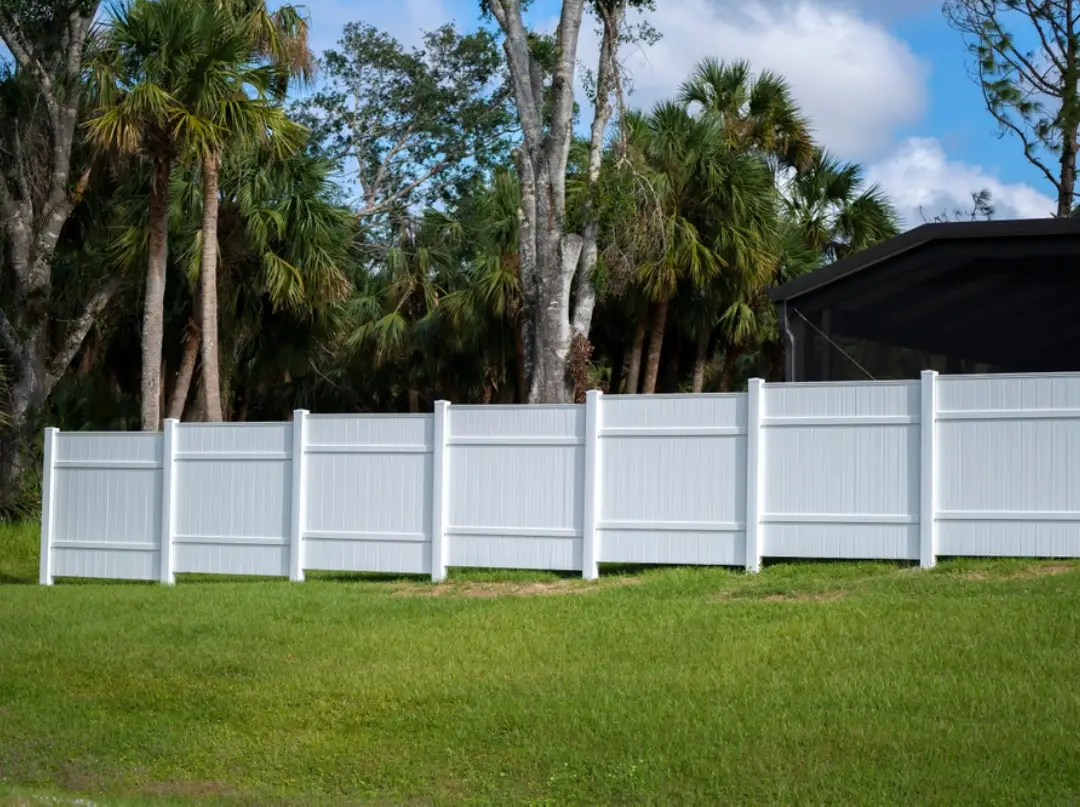 Large white vinyl privacy fence and gates installed along a green lawn backyard.