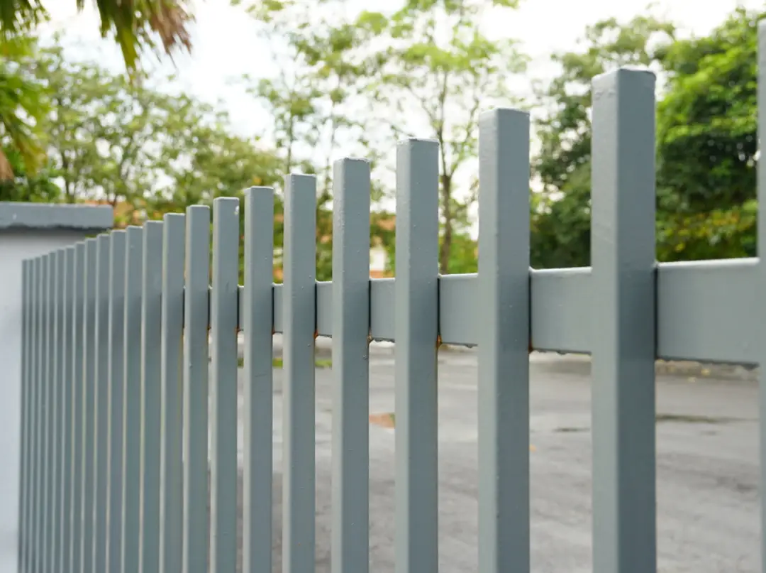 Close-up of a modern gray metal slat fence and gate with vertical square pickets for residential privacy.