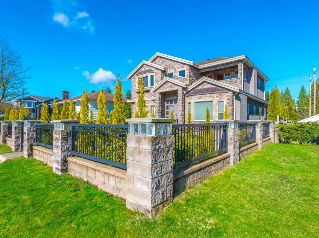 Luxury residential black metal fence and gates with ornate stone pillars and integrated landscaping for a modern estate.