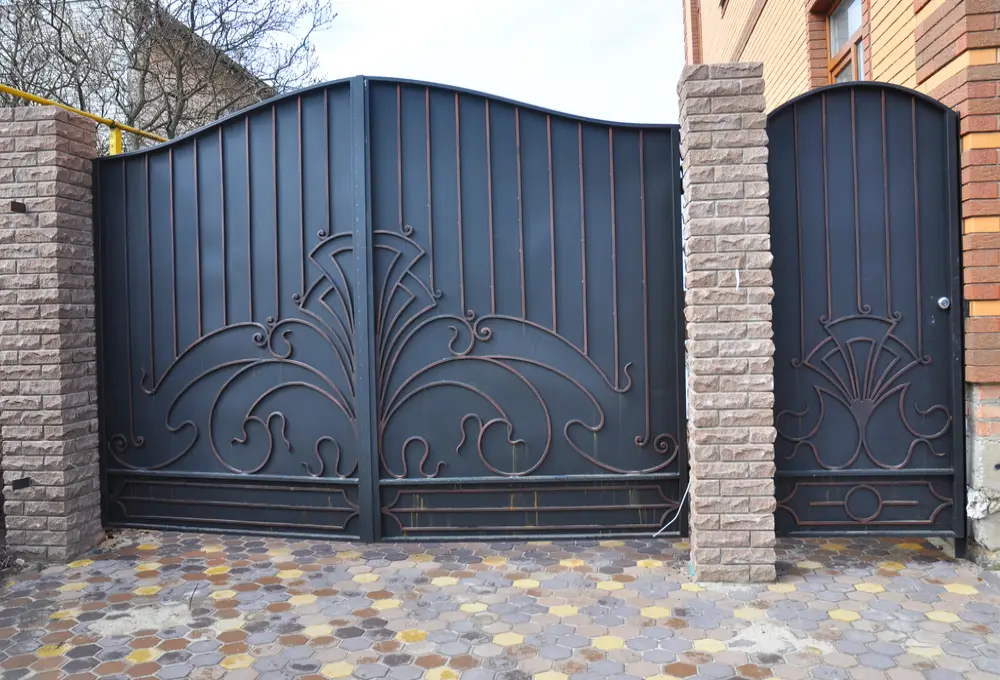 Professional gates installation featuring a large black ornamental wrought iron dual-swing driveway gate and a matching pedestrian side gate between stone pillars.