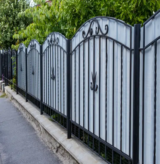 Decorative black wrought iron fence and gates with arched tops and ornamental finials installed on a concrete base.