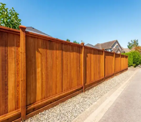 Professional installation of a vertical wood privacy fence and gates with a rich redwood stain along a residential driveway.